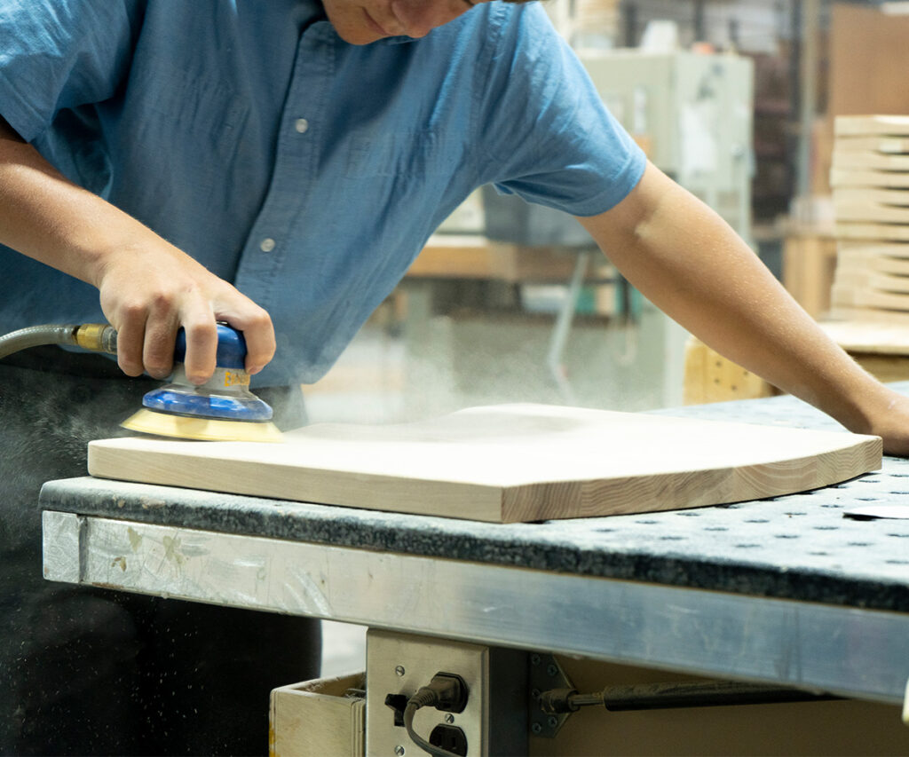 Custom Amish furniture maker sanding a solid wood panel in the workshop.
