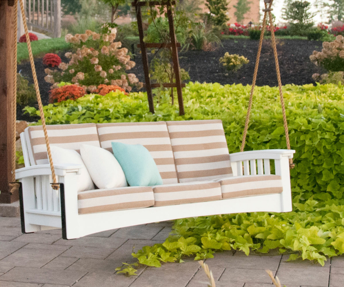 Poly vs. Wood Outdoor Furniture: Which Should You Choose? 2 White poly porch swing with striped cushions in a landscaped patio garden