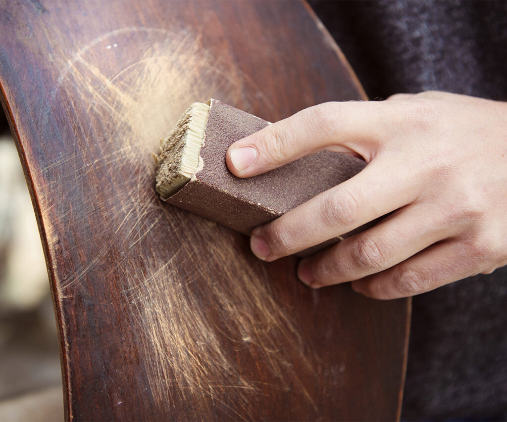 Hand sanding scratches on a chair—solid wood furniture care step.