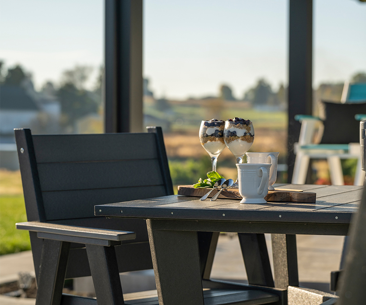 Poly vs. Wood Outdoor Furniture: Which Should You Choose? 4 Black poly patio dining set with desserts and coffee on a covered porch